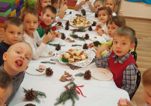 Dzieci jedzą słodki poczęstunek przy świątecznym stole.